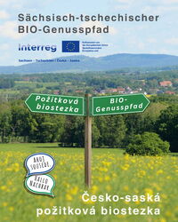 Wegweiser in ländlicher Landschaft mit den Beschriftungen „BIO-Genusspfad“ und „Požitková biostezka“ vor Wiesen und Hügeln – Hinweis auf den sächsisch-tschechischen BIO-Genusspfad.