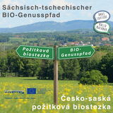Wegweiser mit den Richtungen „BIO-Genusspfad“ und „Požitková biostezka“ in einer blühenden Landschaft – Symbol für deutsch-tschechische Zusammenarbeit im Bio-Tourismus.