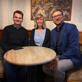 Drei Personen sitzen an einem Tisch.